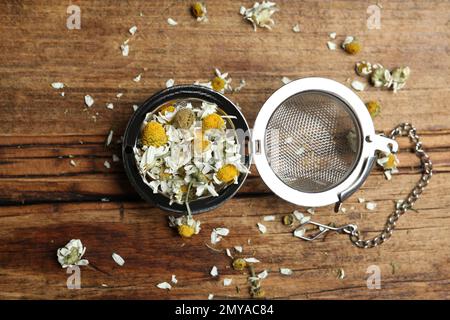 Fiori di camomilla asciutti in infusore su tavolo di legno, piatto Foto Stock