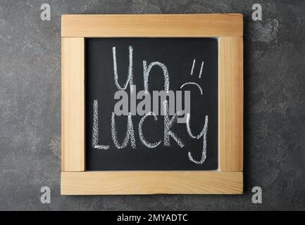 Lavagna con la parola SFORTUNATO e triste faccia su sfondo di pietra grigia, vista dall'alto Foto Stock