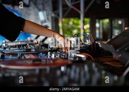 DJ femminile suona musica techno con giradischi in vinile in un bar. Mani di una giovane donna che mescola record sul palco Foto Stock