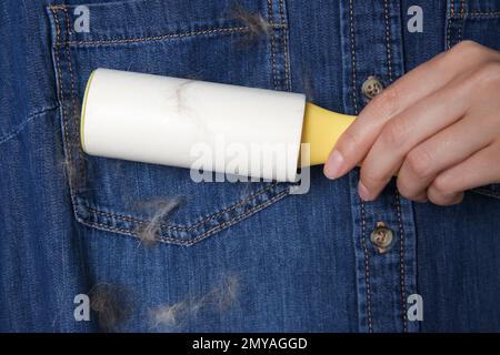 Donna che rimuove i capelli dalla camicia in denim con rullo per pelucchi, primo piano Foto Stock