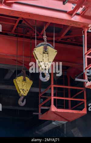 due gru gialle per impieghi pesanti sono appese alle loro funi da un telaio in acciaio rosso di questa vecchia gru industriale Foto Stock