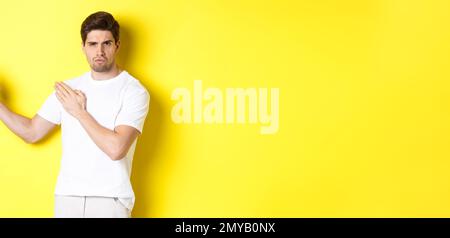 Uomo che mostra abilità kung-fu, arti marziali movimento ninja, in piedi in bianco t-shirt pronto a combattere, in piedi su sfondo giallo Foto Stock