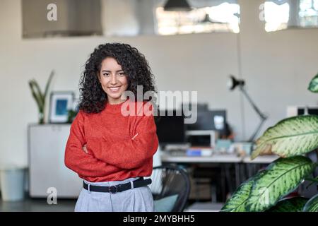 Giovane donna di affari latina sorridente leader in piedi in ufficio, ritratto. Foto Stock