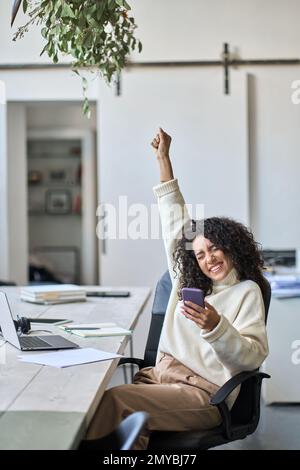 Euforica giovane lavoratrice in possesso di cellulare per celebrare la vittoria. Foto Stock