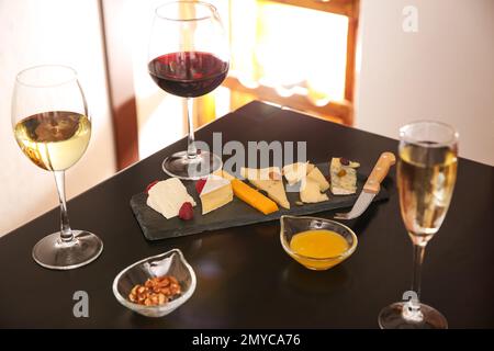 Diversi formaggi deliziosi con spuntini e bicchieri di vino a tavola Foto Stock