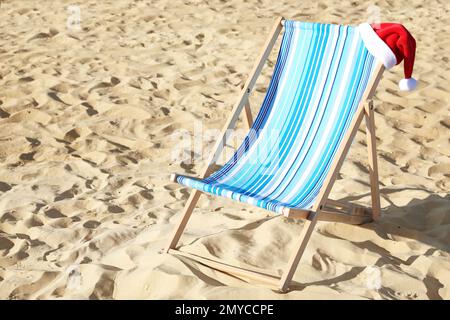 Sedia a sdraio con cappello Babbo Natale sulla spiaggia sabbiosa. Vacanze di Natale Foto Stock