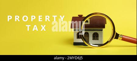 Tassa di proprietà del testo vicino lente d'ingrandimento e modello della casa su sfondo giallo. Design del banner Foto Stock