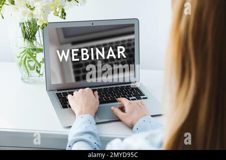 Donna che lavora su un notebook moderno al tavolo bianco al chiuso, primo piano. Webinar aziendale Foto Stock