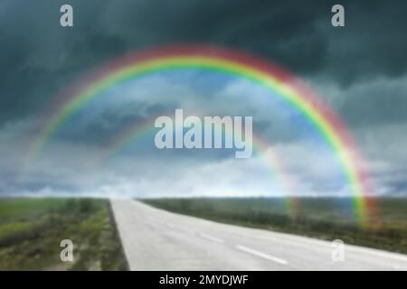 Incredibile doppio arcobaleno sulla strada di campagna sotto il cielo tempestoso, vista offuscata Foto Stock