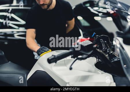 Un esperto di dettaglio di auto irriconoscibile che utilizza una spugna per una motocicletta bianca profonda e pulita. Scatto medio in interni. Spazio di copia. Foto di alta qualità Foto Stock