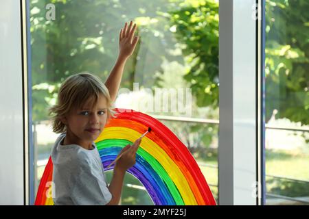 Bambino che disegna arcobaleno sulla finestra. Concetto di soggiorno a casa Foto Stock