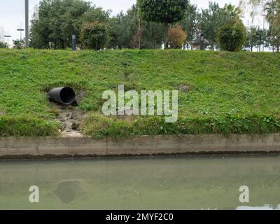 Il tubo sporge dalla pendenza. Drenaggio dell'acqua dalle acque piovane nel fiume. Industria. Sistema di drenaggio in città. Foto Stock