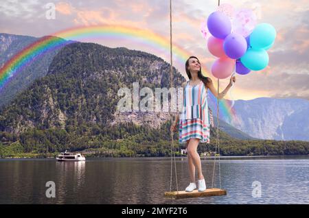 Il mondo dei sogni. Giovane donna con palloncini luminosi che oscillano, montagne e lago sullo sfondo Foto Stock