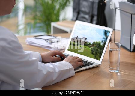 Servizio online agenzia immobiliare. Medico scegliendo nuova casa via laptop, primo piano Foto Stock