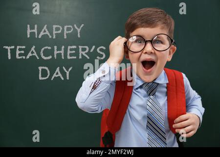 Emotivo bambino che indossa occhiali vicino alla lavagna con testo Happy Teacher's Day Foto Stock