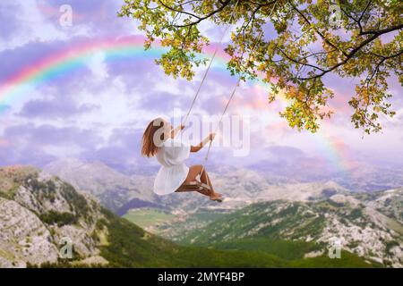 Il mondo dei sogni. Giovane donna che oscilla sulle montagne sotto il cielo del tramonto Foto Stock