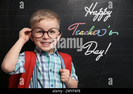 Cute bambino piccolo che indossa gli occhiali vicino alla lavagna con testo Happy Teacher's Day Foto Stock