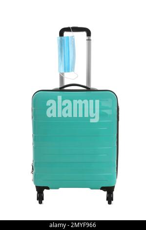 Elegante valigia turchese e maschera protettiva su sfondo bianco. Viaggiare durante la pandemia di coronavirus Foto Stock
