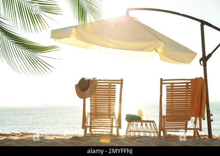 Sedie a sdraio in legno, stativo in vimini e ombrellone sulla spiaggia di sabbia. Vacanze estive Foto Stock