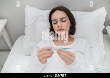 Donna malata con febbre che controlla la sua temperatura, che riposa a letto Foto Stock