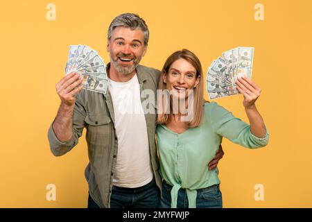 Tanti soldi, gioia della vittoria. Felice coppia caucasica di mezza età che tiene molti dollari, esprimendo emozioni di successo Foto Stock