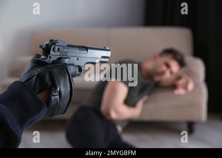 Uomo che punta la vittima con la pistola in casa, primo piano. Criminale pericoloso Foto Stock