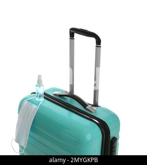 Elegante valigia turchese, spray antisettico e maschera protettiva su sfondo bianco. Viaggiare durante la pandemia di coronavirus Foto Stock
