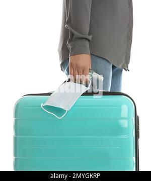 Donna con valigia, spray antisettico e maschera protettiva su sfondo bianco, primo piano. Viaggiare durante la pandemia di coronavirus Foto Stock