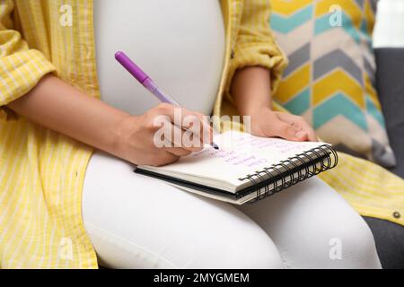 Donna incinta scrivere la lista dei nomi del bambino, primo piano Foto Stock