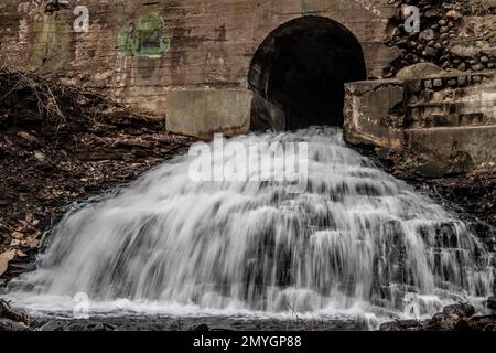 Lunga cascata di esposizione che scorre attraverso un tunnel sotto una strada in una giornata di primavera nel centro di Marine on St Croix, Minnesota USA. Foto Stock