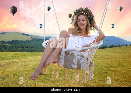 Il mondo dei sogni. Giovane donna che oscilla sul verde prato vicino alle montagne, palloncini ad aria calda nel cielo del tramonto sullo sfondo Foto Stock