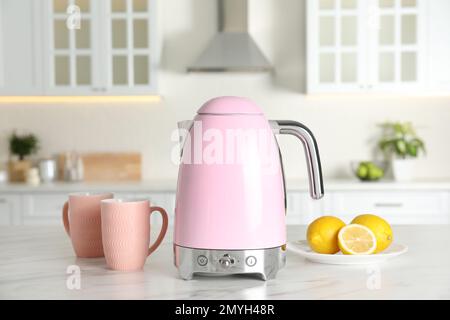 Bollitore elettrico moderno, tazze e limoni sul tavolo in cucina Foto Stock