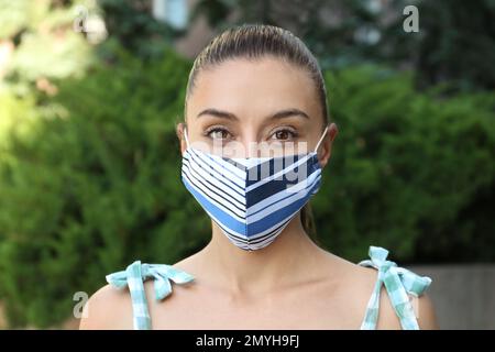 Donna che indossa una maschera di stoffa fatta a mano all'aperto. Dispositivi di protezione individuale durante la pandemia COVID-19 Foto Stock