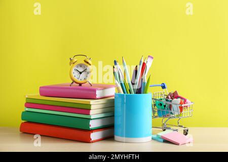 Cancelleria diversa scuola e sveglia sul tavolo su sfondo giallo. Ritorno a scuola Foto Stock