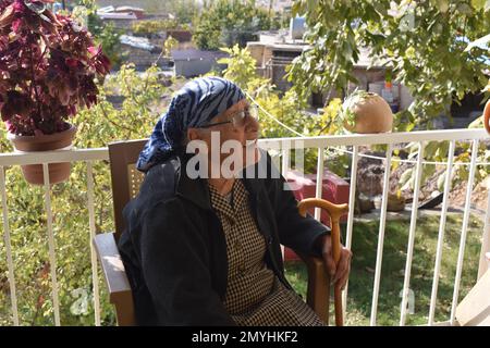 Una donna anziana seduta sul suo portico in un giorno autunnale wam nel nord dell'Iraq. Foto Stock
