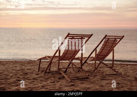 Sedie a sdraio in legno sulla spiaggia sabbiosa al tramonto. Vacanze estive Foto Stock