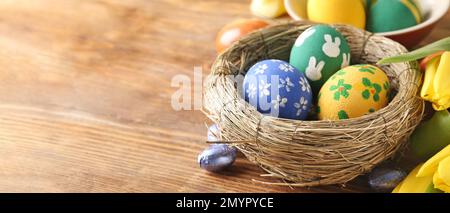 Nido con uova di Pasqua dipinte e caramelle su sfondo di legno con spazio per il testo Foto Stock