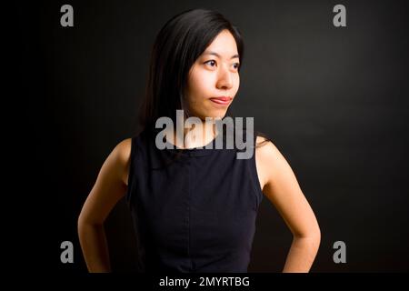 Profilo di atletica giovane donna asiatica con mani sui fianchi | sfondo nero | vestiti da allenamento Foto Stock