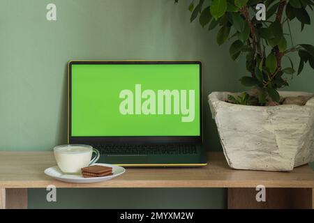 computer portatile con yogurt con schermo verde e biscotti su un tavolo in una stanza a casa Foto Stock