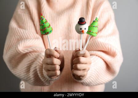 Donna che tiene deliziosi papi di torta di Natale a tema su sfondo grigio, primo piano Foto Stock