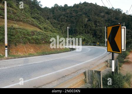 Segnale stradale che avverte una curva stretta di fronte su una strada vuota. Foto Stock