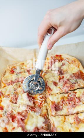 Succulenta e deliziosa fetta di pizza con prosciutto, cipolla e formaggio. Lo chef taglia la pizza a pezzi con un coltello. Cucinare la pizza a casa Foto Stock