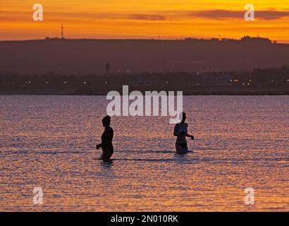 Portobello, Edimburgo, Scozia, Regno Unito 5th febbraio 2023. Cielo fresco e colorato all'alba sopra il Firth of Forth e la spiaggia di mare per le poche persone fuori a testimoniarlo. Temperatura 1 gradi centigradi con ghiaccio su superfici bagnate e parabrezza per auto. Nella foto: Due nuotatori d'acqua fredda nel Firth of Forth per un tuffo freddo. Credito: Archwhite Foto Stock