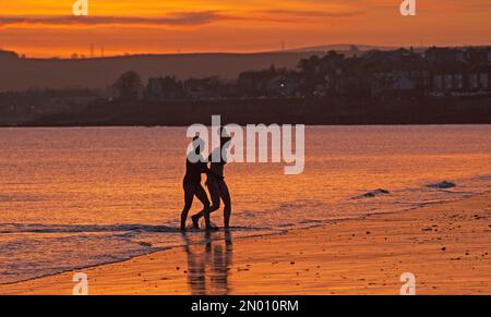 Portobello, Edimburgo, Scozia, Regno Unito 5th febbraio 2023. Cielo fresco e colorato all'alba sopra il Firth of Forth e la spiaggia di mare per le poche persone fuori a testimoniarlo. Temperatura 1 gradi centigradi con ghiaccio su superfici bagnate e parabrezza per auto. Nella foto: Due nuotatori d'acqua fredda nel Firth of Forth per un tuffo freddo. Credito: Archwhite Foto Stock