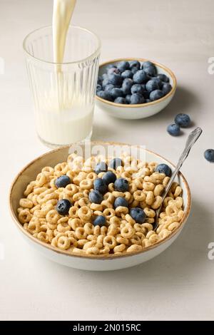 ciotola di cereali per la colazione, anelli di miele e latte sul tavolo da cucina bianco Foto Stock