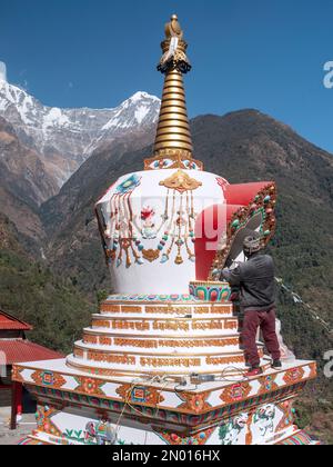 Chhomrong, Nepal. Uomo che finisce gli ultimi dettagli del nuovo villaggio stupa. Annapurna Sud sullo sfondo. Foto Stock
