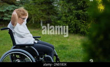 Donna caucasica anziana che fa esercizi mentre si siede su una sedia a rotelle all'aperto. Foto Stock