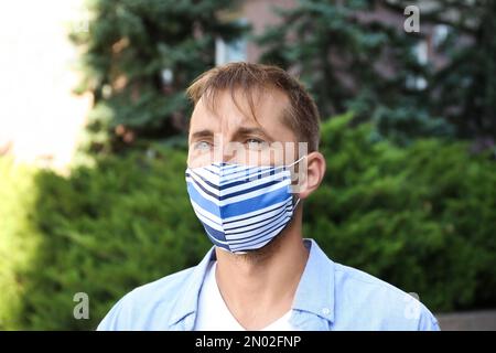 Uomo che indossa una maschera in tessuto fatta a mano all'aperto. Dispositivi di protezione individuale durante la pandemia COVID-19 Foto Stock