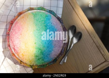 Rasatore di ghiaccio arcobaleno in ciotola di vetro da dessert e cucchiai su tavolo di legno, piatto Foto Stock