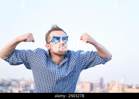 Fists pompato o superpotenza, aggressività concetto di emozione. Uomo caucasico in camicia da notte e maschera blu supereroe con gesto di forza e faccia arrabbiata. Immagini di alta qualità Foto Stock